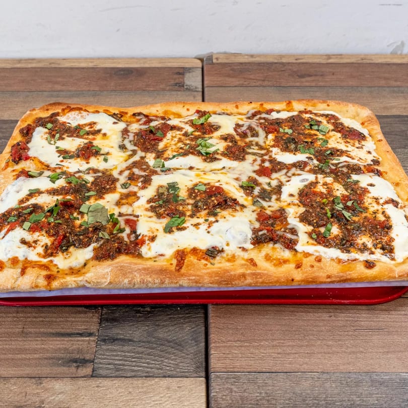 A rectangular Pizza Chop pizza with white cheese, red sauce, and green herbs on a red tray.