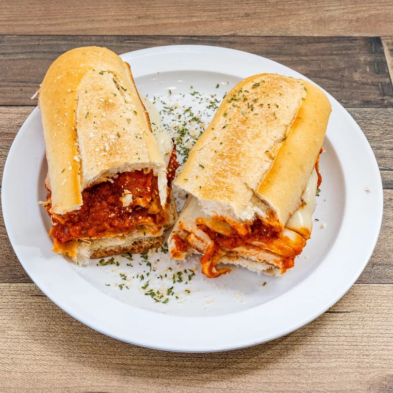 Two halves of a meatball sub sandwich with melted cheese and marinara sauce on a white plate.
