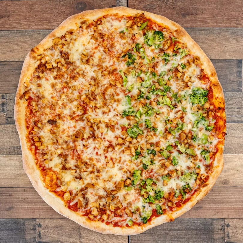 Whole Pizza Chop pizza, half with chicken and half with broccoli, on a wooden table.