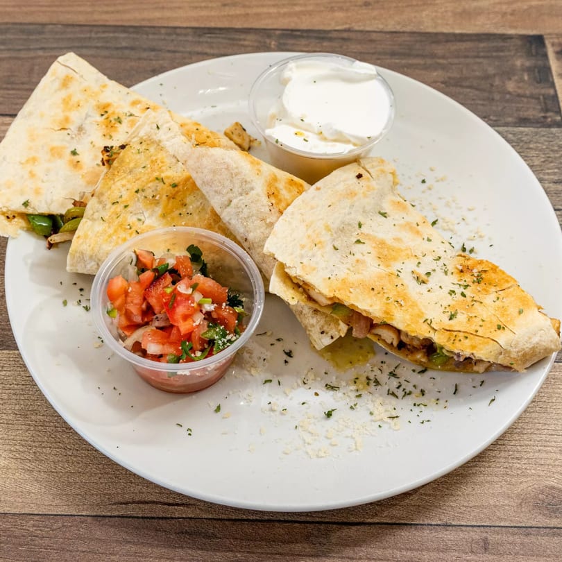 Chicken quesadillas with salsa and sour cream on a white plate from Pizza Chop.